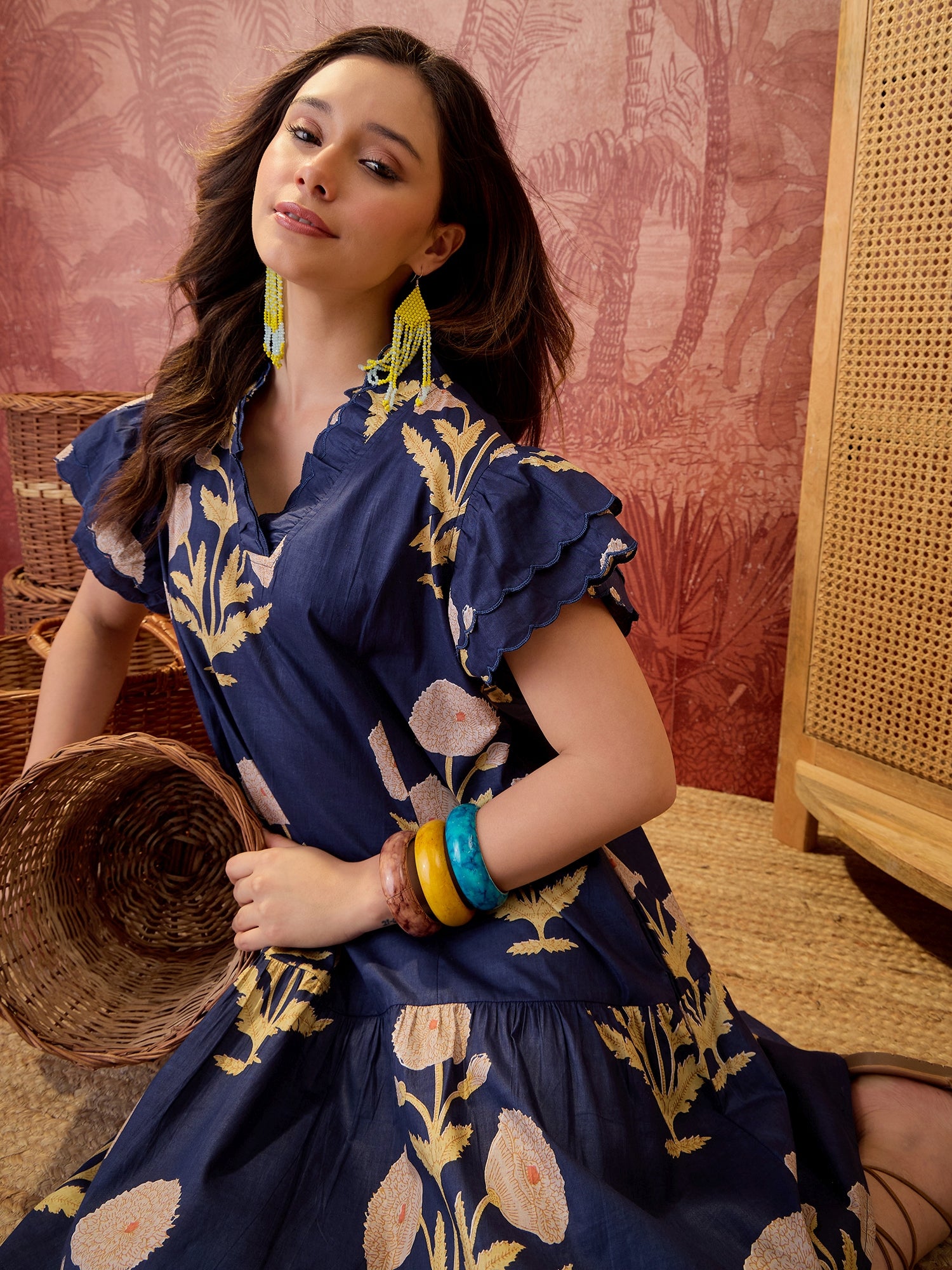 Woman wearing a navy blue floral printed relaxed mini dress with ruffle sleeves and scalloped neckline.