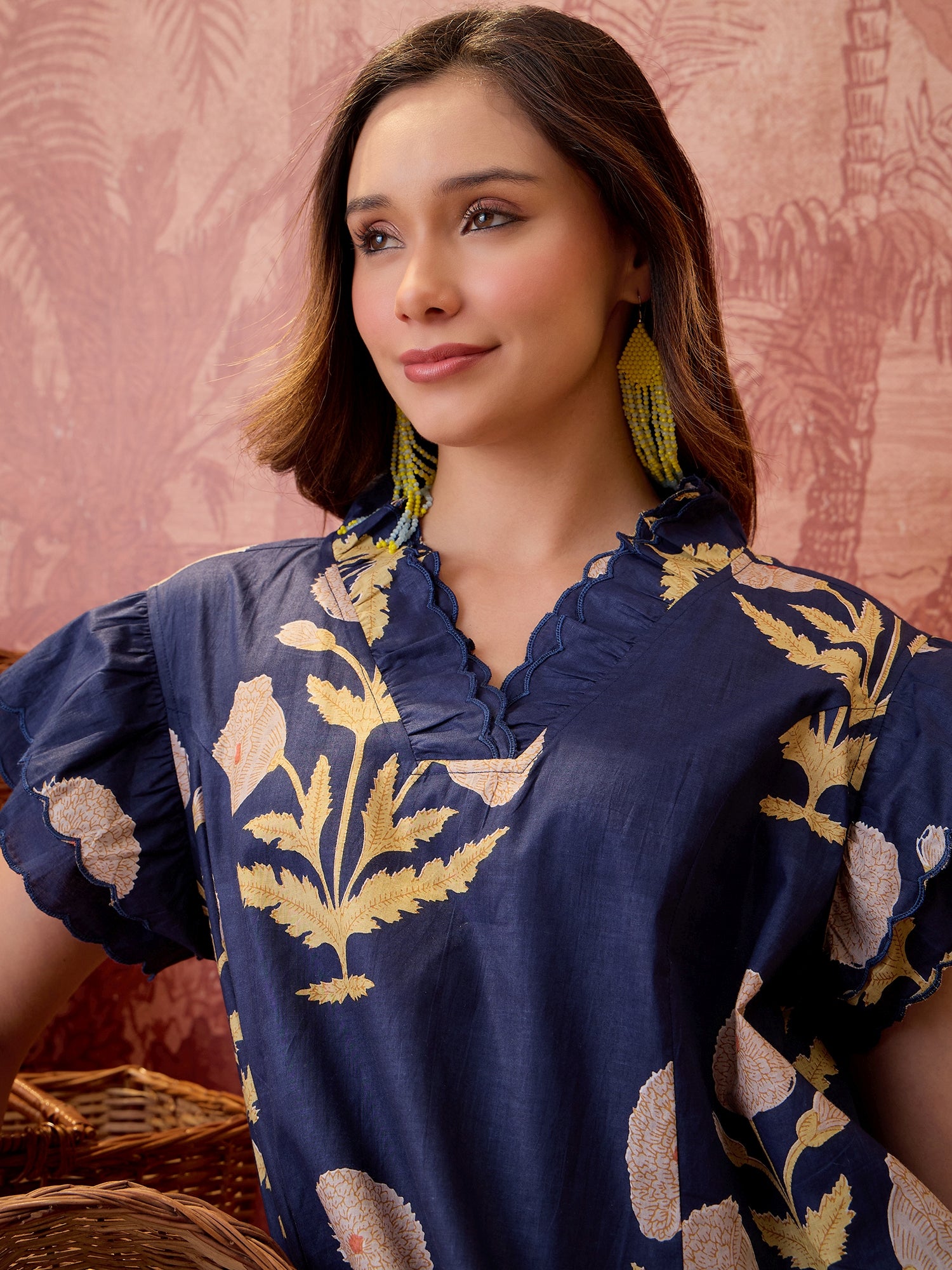 Woman wearing a navy blue floral printed relaxed mini dress with ruffle sleeves and scalloped neckline.