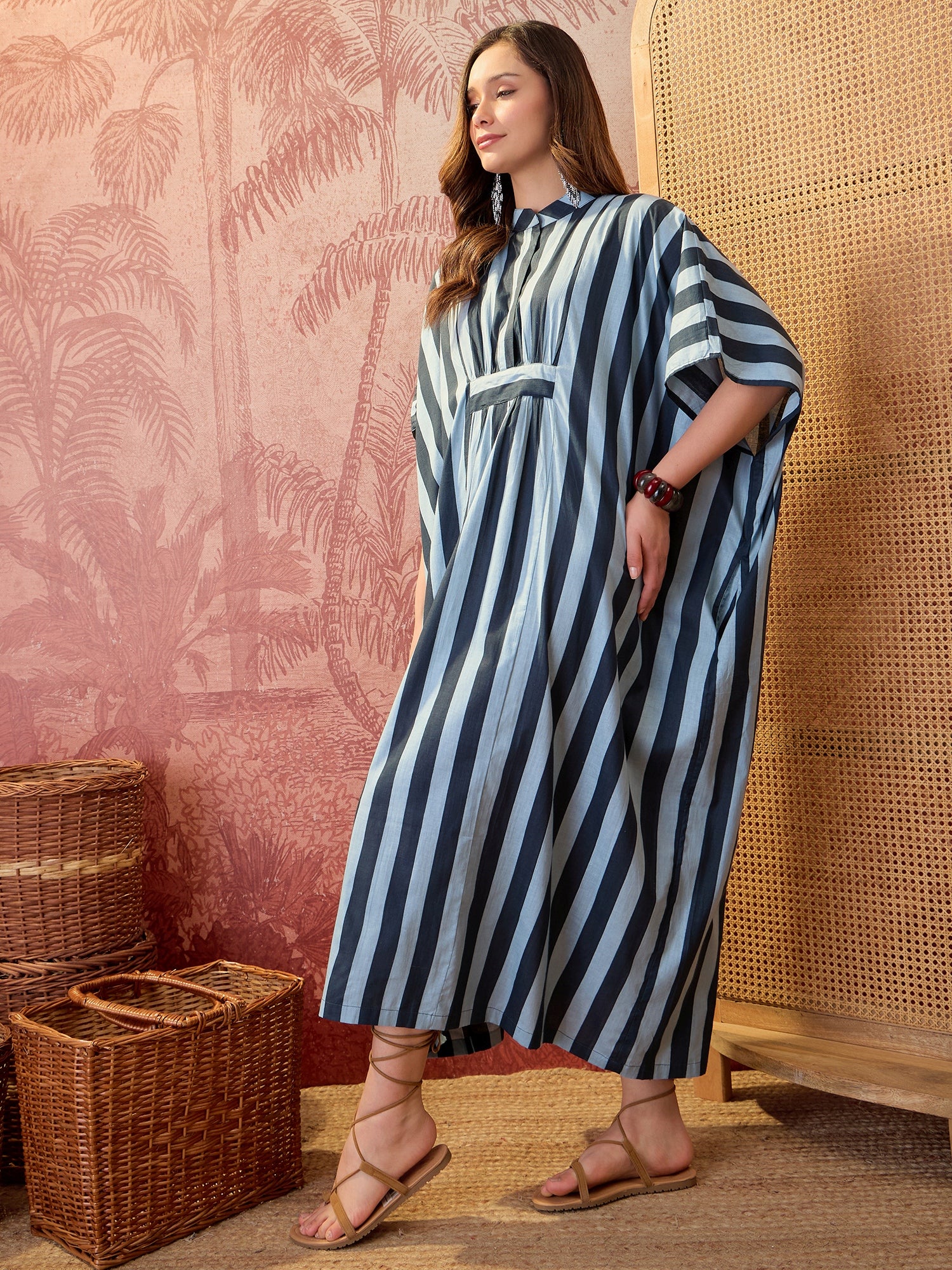 Woman wearing a blue striped oversized kaftan maxi dress with flowing silhouette and vertical stripe pattern.