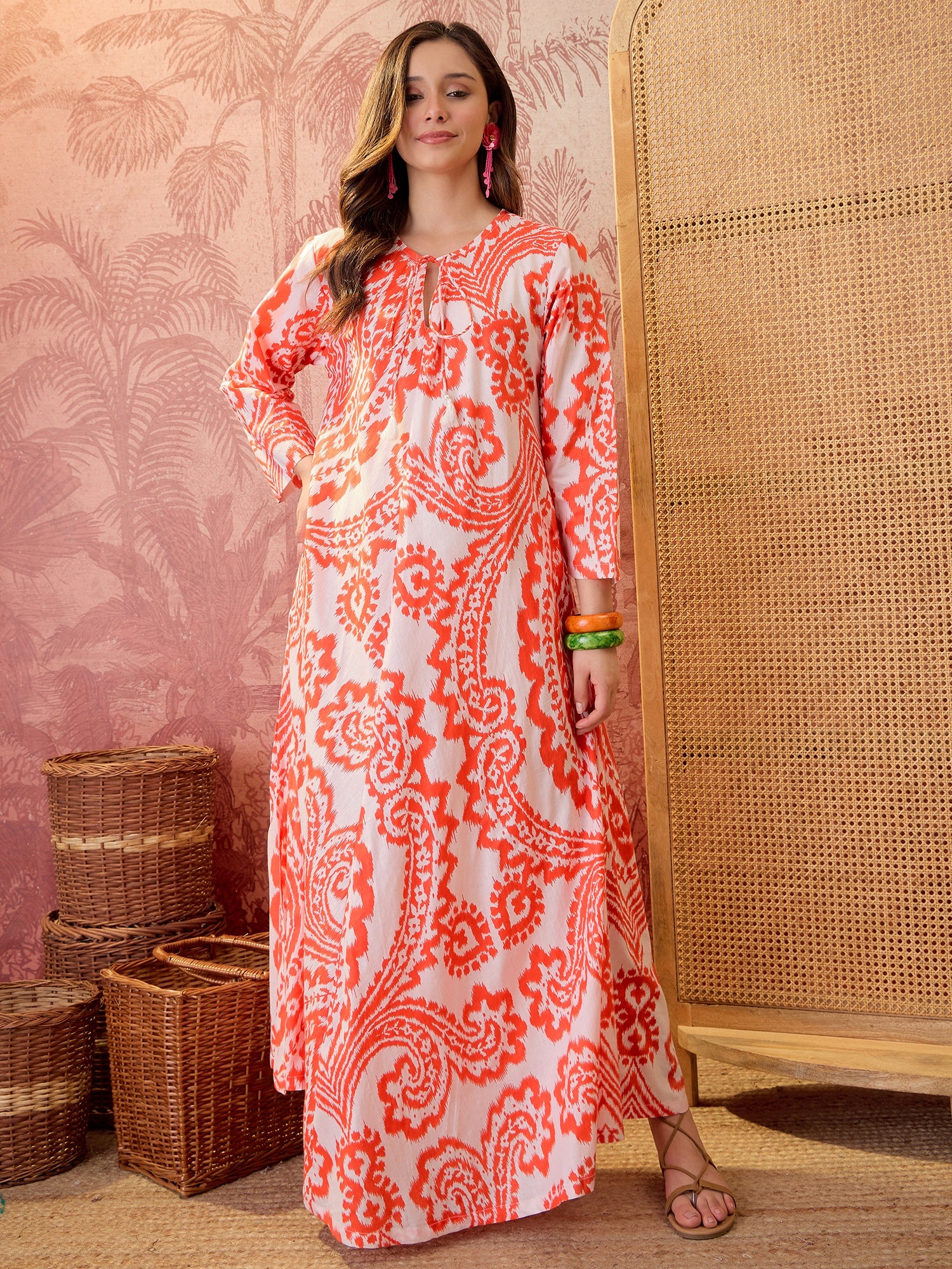 Woman wearing a coral paisley printed relaxed maxi dress with tie-up neckline and flowing silhouette.