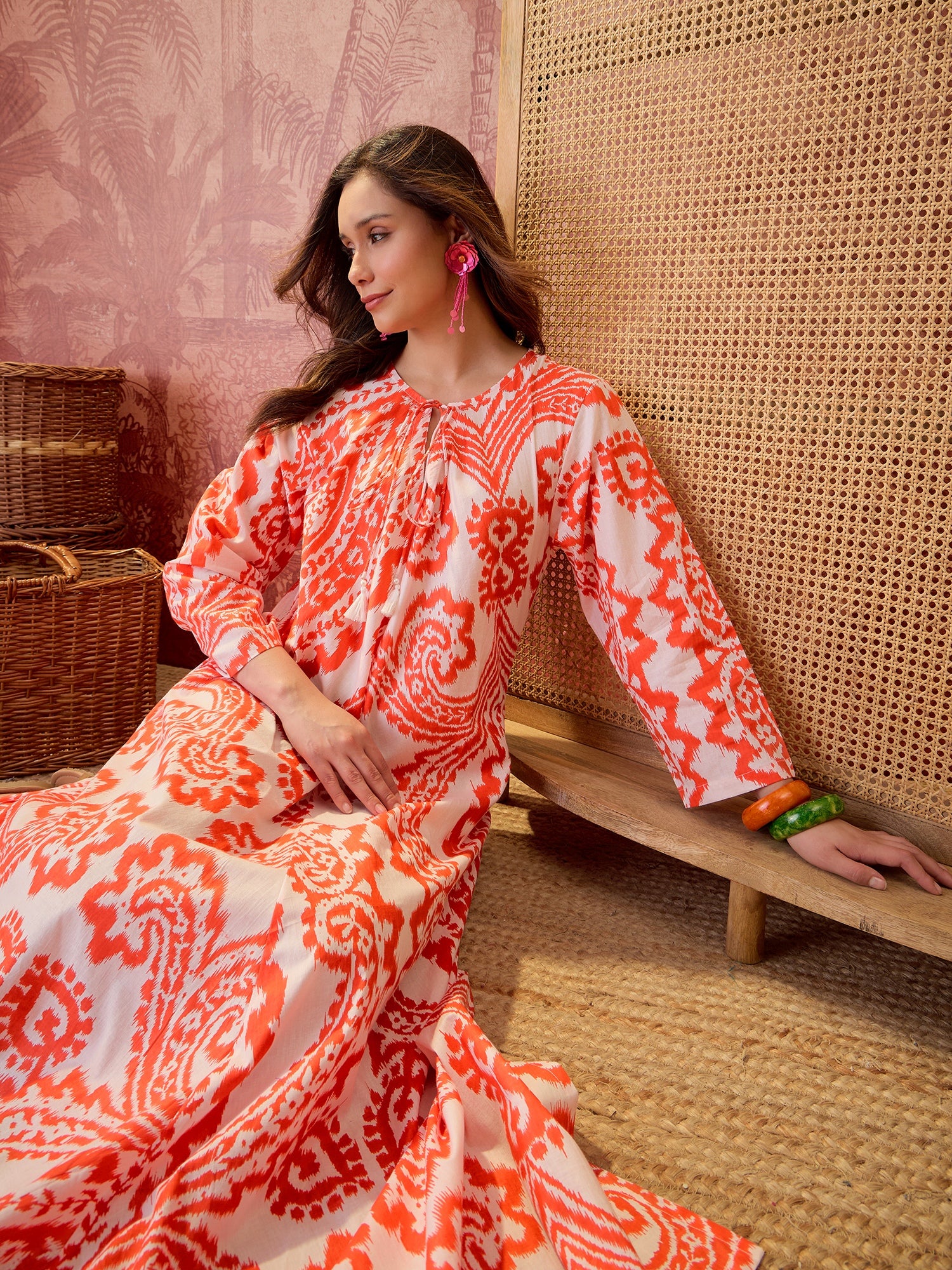 Woman wearing a coral paisley printed relaxed maxi dress with tie-up neckline and flowing silhouette.